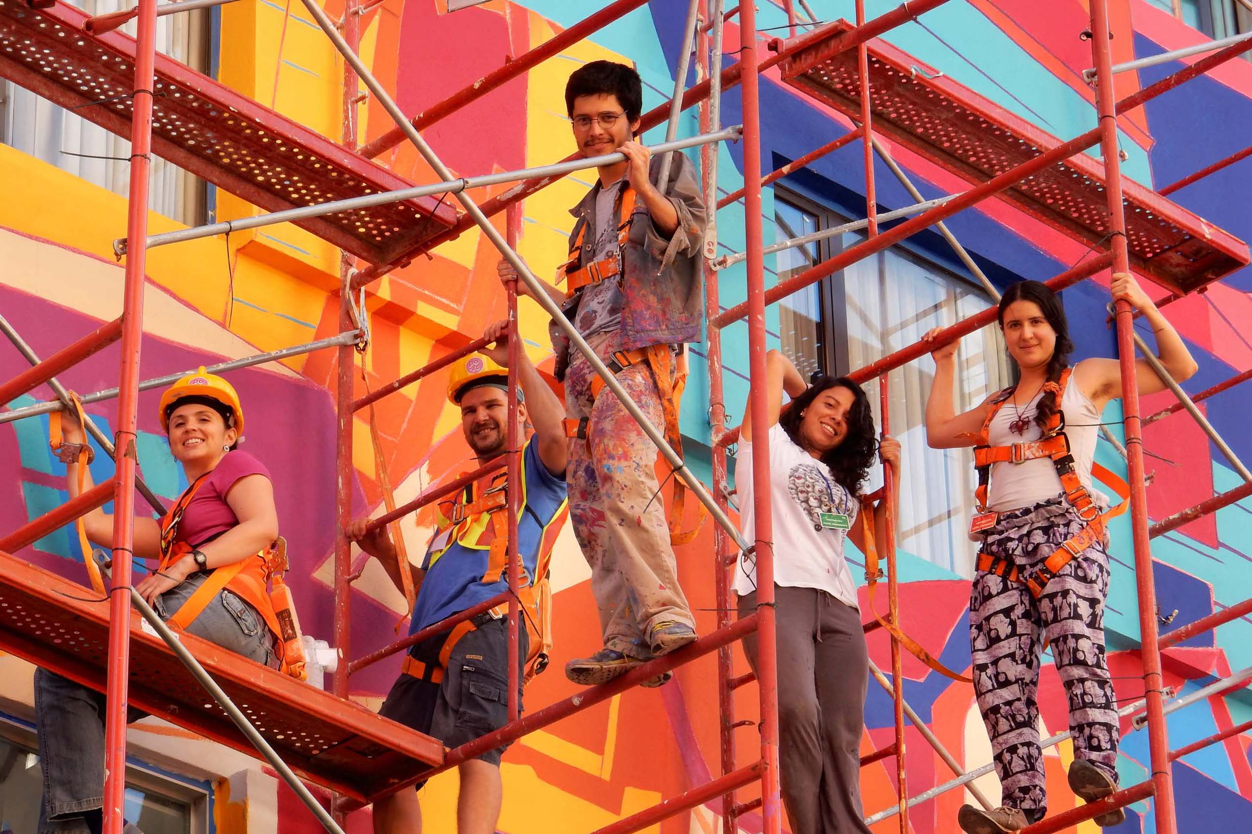 Artistas sobre andamios frente a un mural en proceso